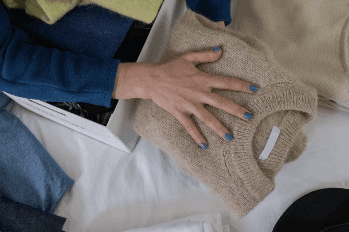 Main rangeant pull plié dans penderie organisée avec vêtements bleus et beiges