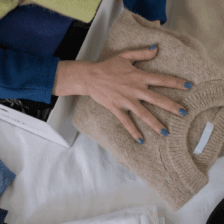 Main rangeant pull plié dans penderie organisée avec vêtements bleus et beiges