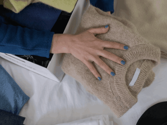 Main rangeant pull plié dans penderie organisée avec vêtements bleus et beiges