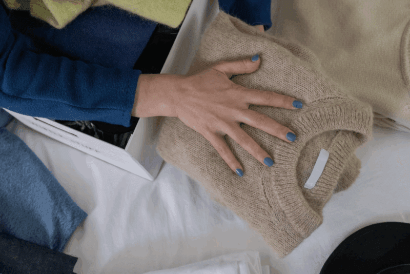Main rangeant pull plié dans penderie organisée avec vêtements bleus et beiges