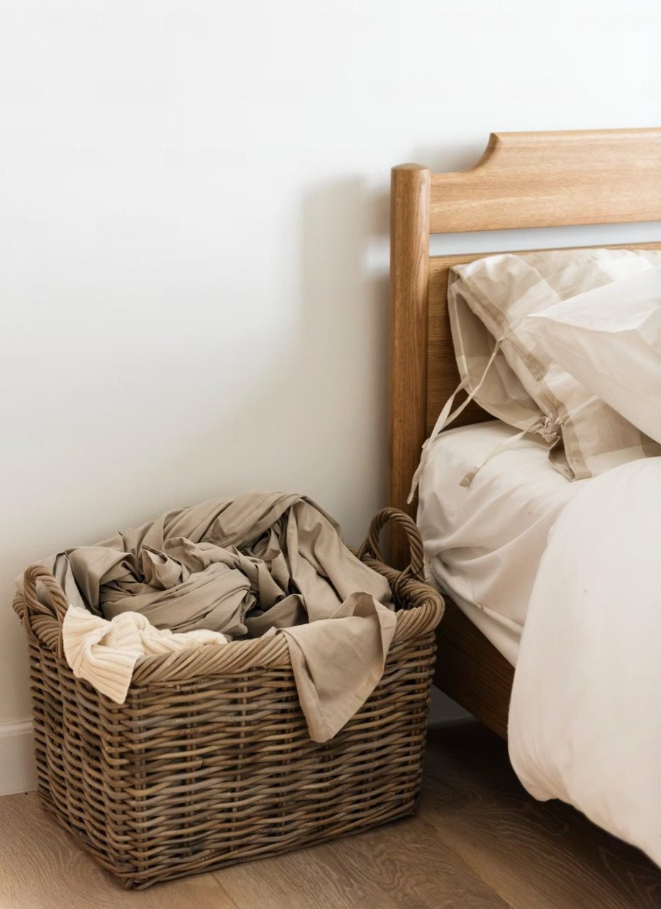Panier en osier naturel posé sur une étagère blanche, contenant quelques objets bien rangés
