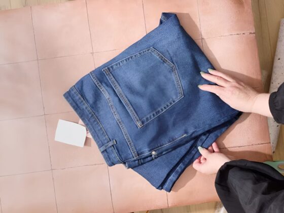 Tutoriel pliage jean méthode KonMari vue du dessus avec mains positionnant jean bleu denim sur surface rose pour rangement vertical tiroir