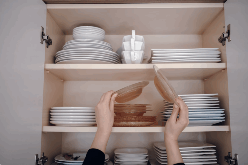Placard de cuisine organisé avec tupperware et boîtes alimentaires empilés et rangés par taille sur des étagères en bois clair